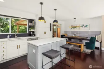 This stylish kitchen and dining area boasts modern pendant lighting, sleek quartz countertops, and custom cabinetry with brass hardware. The cozy built-in banquette and open layout create a perfect space for casual dining or entertaining, with easy access to the private outdoor deck.
