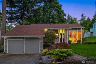 A wide driveway leads to a spacious two-car garage, while thoughtfully placed shrubs and seasonal blooms add warmth and character. The home's modern yet welcoming facade is bathed in natural light, setting the tone for the comfort and style that await inside.