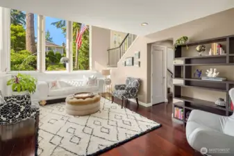 Bathed in natural light, this stunning living room features soaring double-height ceilings and expansive picture windows framing lush greenery. Elegant design details include a tufted sofa, statement lighting, and a graceful staircase—creating a warm, welcoming first impression.