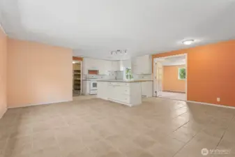 Step inside and you’re greeted by living room walls in autumn shades that balance cozy and bold, paired with a white-on-white kitchen that plays it clean. The island gives you a seat for coffee or chats with the cook, and French doors lead you into the next room with a little drama.