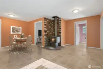 On this side of the living room, the star is the wood stove perched on a brick hearth that layers terracotta, cream, and deep tones. The scale of the room means you’ve got space to spread out, and you see the connections to more bedrooms beyond, which keeps the floorplan feeling open and livable.