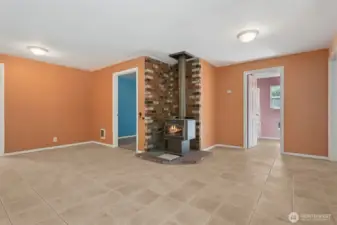 On this side of the living room, the star is the wood stove perched on a brick hearth that layers terracotta, cream, and deep tones. The scale of the room means you’ve got space to spread out, and you see the connections to more bedrooms beyond, which keeps the floorplan feeling open and livable.