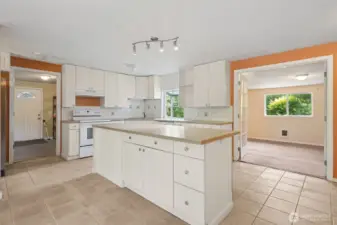 The kitchen keeps it classic with white shaker-style cabinets, silver hardware, and a clean tile backsplash. White appliances blend in, while a corner sink sits under a garden shelf window that’s basically begging for fresh herbs. The back door carries the same arched glass detail as the front, and through the French doors you’ve got flex space that works as a third bedroom or whatever you need.