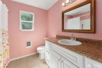 This bath feels polished, with rose-toned walls that make mornings feel less harsh, a long vanity with storage so the counter isn’t buried, and a wood-framed mirror that pulls it all together. The window adds daylight and fresh air, and the full shower-tub surround means no one has to compromise.