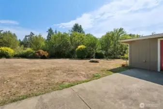 The backyard is level and lovely, edged with mature landscaping that frames the space without taking it over. A concrete patio gives you room to spread out seating in multiple zones, so you’re not cramming everyone around one table. Trees and shrubs add privacy, making it feel like your own green retreat.