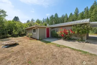 Blooming plants frame the patio that wraps to the side of the house, giving the backyard real curb appeal where it counts. The lawn is in late-summer vacation mode, but the trees and shrubs pick up the slack, creating privacy and a tucked-away vibe.