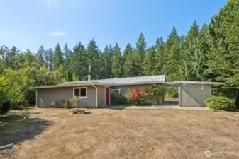 From the landscaped edge you see the back of the house, complete with a breezeway that connects to the garden shed so tools never feel far away. The metal roof tops it all, delivering durability and peace of mind that shingles can only dream about.