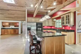 View of main kitchen towards wet bar and entry hall, you will love all the wood including amazing beams in this home. Granite counters, plenty of counter space, hickory cabinets, lots of lighting, heated floors!