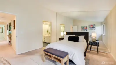The primary bedroom features a stunning wall-to-wall mirror behind the bed, enhancing both the sense of space and natural light.