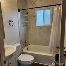 Full bath in hallway with newer upgrades, flooring, sink, tub, cabinets, marble tile and   window