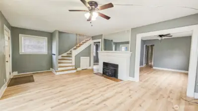 Brand new flooring throughout!  Living Rm with wood-burning fireplace.  A view into the formal Dining Rm, and stairs to the upper floor.