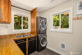 Laundry room right off the kitchen has Electrolux washer/dryer set, sustainable Kirei counters, a strong, lightweight, environmentally friendly substitute for a wood countertop, carpet tiles (over ceramic tiles), storage galore with cherry cabinets, a double basin sink, and access to the garage