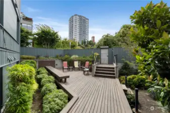 This beautifully designed common area deck offers a serene retreat. Surrounded by lush greenery, the space is perfect for outdoor gatherings or quiet relaxation. The expansive teak deck features ample seating, including a built-in bench that complements the modern design. Raised planters with vibrant foliage add a touch of nature, creating a tranquil environment for residents to enjoy. Whether hosting a small get-together or simply unwinding with a book, this deck is a versatile outdoor space that enhances the community living experience.