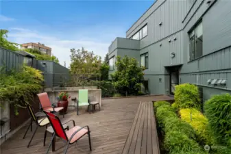 This beautifully designed common area deck offers a serene retreat. Surrounded by lush greenery, the space is perfect for outdoor gatherings or quiet relaxation. The expansive teak deck features ample seating, including a built-in bench that complements the modern design. Raised planters with vibrant foliage add a touch of nature, creating a tranquil environment for residents to enjoy. Whether hosting a small get-together or simply unwinding with a book, this deck is a versatile outdoor space that enhances the community living experience.