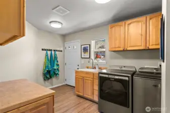 Spacious utility room with washer and dryer included, featuring a laundry sink, ample storage, and direct exterior access.