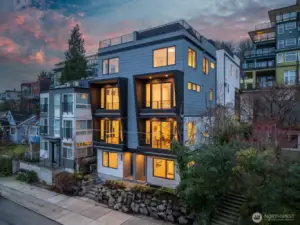 Twilight curb appeal: modern lines glow against a rose-colored sky, showcasing tiered balconies and expansive windows. Photos are of model home 2009B.