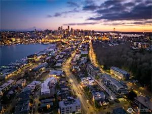 Twilight aerial: Lake Union glitters below as Seattle’s skyline lights up—proof that your new address sits minutes from South Lake Union offices, marinas, and downtown nightlife. Photos are of model home 2009B.