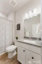 Bright full bathroom featuring quartz countertop, updated lighting, and neutral finishes, along with a tub/shower combo designed for easy everyday care.