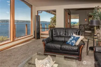 Sweeping views from every part of this home, here in the living room just to the left of the entrance showing wall glass in the media area as well as seeing views all the way into the kitchen area looking at the Mukilteo Ferries.
