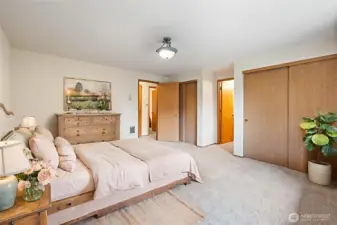 Another view of the primary bedroom, looking towards the dual closets and bathroom entrance. Also virtually staged.