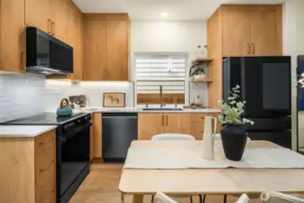 Welcome home! Chef’s kitchen featuring sleek wood cabinetry, high-end black appliances, and contemporary white quartz countertops.