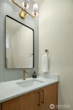 Stylish half-bath featuring a floating wood vanity, designer gold-rimmed mirror, and chic modern lighting.