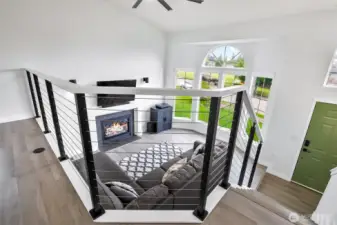 Open railing design overlooking the vaulted living room with gas fireplace and oversized arched windows.