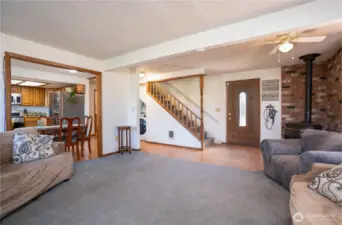 Another view of living room with entry door & propane stove. Stairs lead to upper level with 3 bedrooms and full bathroom
