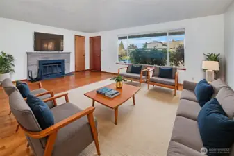 Spacious living room with large North facing window for ample indirectly lighting and wood burning fireplace. (VR staged)