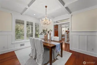 An inviting dining room with a crystal chandelier, coffered ceilings and wainscotting