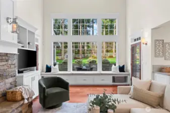 Architecture and nature converge in the grand great room, where soaring vaulted ceilings and floor-to-ceiling windows frame the lush Fox Island landscape. A towering stone fireplace provides a rhythmic warmth, while the integrated window seat offers a bespoke "stay awhile" nook for afternoon repose.
