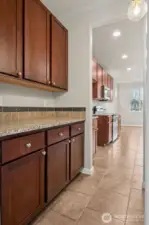 This butler’s pantry is doing the most, and we love that for it. Granite countertops give you real prep space, while the rich coffee-toned shaker cabinetry brings warmth and serious storage. Tile flooring keeps things practical, especially for high traffic moments or enthusiastic coffee routines. Straight ahead the kitchen stays within arm’s reach. It’s the kind of in-between space that quietly upgrades how the whole house functions.