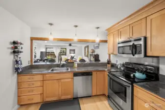 Large kitchen with stainless steel appliances and granite counters overlooks the living area