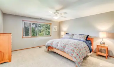 Generous primary bedroom space with large window framing beautifully curated backyard.
