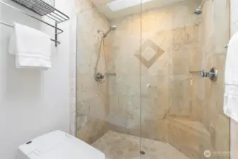 Stylish travertine tile, frameless glass, and heated bidet toilet
