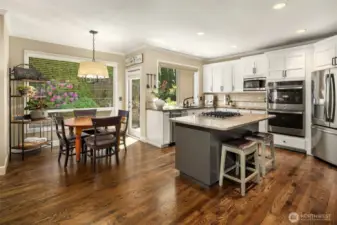Wide angle photo of kitchen and eating area shows off the beautiful hardwood floors, ample kitchen space and updated, stainless appliances.