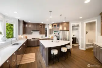 Sunlit kitchen with a bay window, custom tiled full-height backsplash, quartz countertops, soft-close drawers, flush to-ceiling cabinets, glass cabinets with lighting, and commercial grade stove.