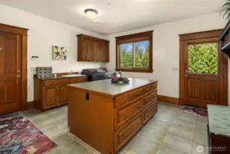 A spectacular laundry room / mud room has loads of cabinet space, center island, fold down ironing board, sink area, and full size washer & dryer, and tiled floors. The door to the right leads out to the side yard and driveway. The door to the left goes into  the garage.