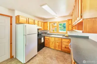 Charming country-style kitchen with warm pine cabinetry and a bright window over the sink. The side door leads to a utility room with access to the garage—perfect for everyday convenience.