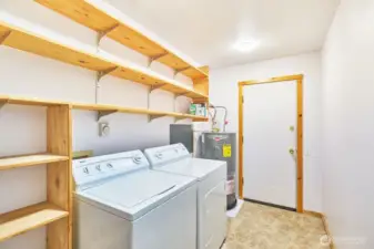 Large laundry room with storage shelves and brand new hot water heater. Door leads to garage/workshop.