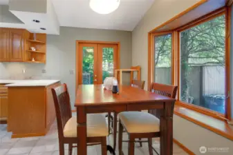 Wood-wrapped windows and a bright bay window fill the space with natural light, complemented by tile floors and a dining area conveniently located next to the kitchen.