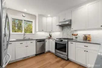 Kitchen with white cabinetry, tasteful tile backsplash, natural gas range with hood, stylish solid surface countertops, under cabinet accent lighting & shelving niches.
