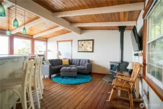 Living room has beautiful vaulted ceiling with exposed beams & tongue & groove wood floors with wood burning stove. The dining room has a wall of windows with incredible Southerly view.