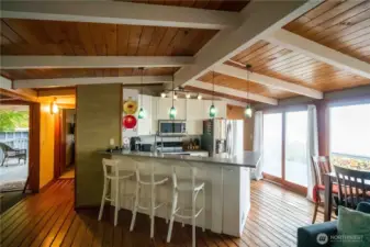 Open concept living area offers beautiful vaulted ceiling with exposed beams & tongue & groove wood floors with wood burning stove. The dining room has a wall of windows with incredible Southerly view. Kitchen has wrap around quartz eating.