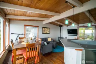Open concept living area offers beautiful vaulted ceiling with exposed beams & tongue & groove wood floors with wood burning stove. The dining room has a wall of windows with incredible Southerly view. Kitchen has wrap around quartz eating.