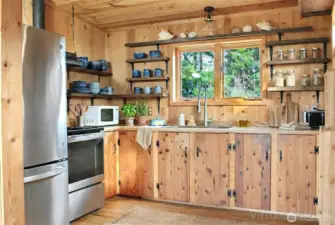 The upstairs kitchen offers a welcoming coastal feel with warm wood cabinetry, open shelving, and a comfortable space for cooking and gathering.