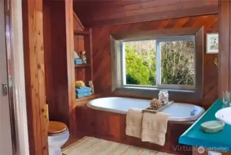 The upstairs bathroom features a warm wood-lined design with a soaking tub, built-in shelving, and a serene, spa-like atmosphere.