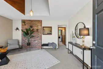 Step into a bright and inviting living room featuring soaring high ceilings and a striking brick accent wall that adds warmth and character.
