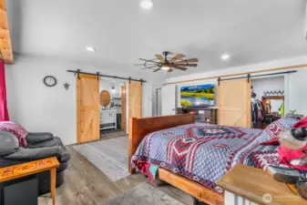 Another view of the primary bedroom downstairs and the walk-in closet as well as the adjoining bathroom. Canned lighting as well as a ceiling fan with light. More wood shelving around the room for pictures.
