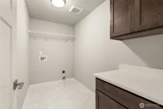 Separate laundry room with a counter, storage cabinets and a storage shelf above appliances.